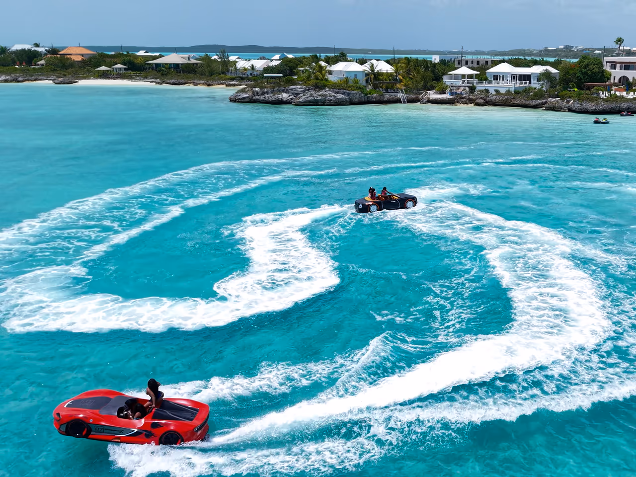 Both Jet Cars, one red and one black, carving white wake spirals across turquoise water, seen from our drone