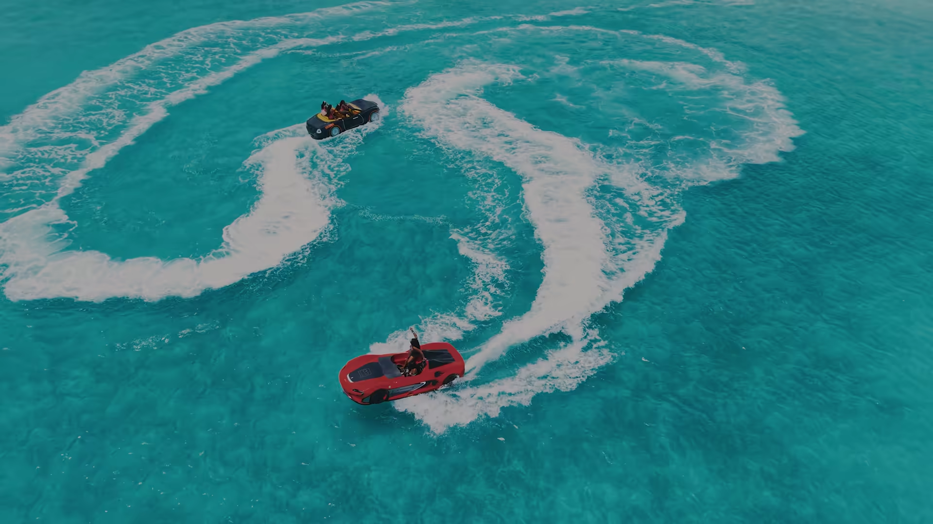 The red 2-seater and the black 4-seater Jet Car carving wide spirals of white wake across turquoise shallows off Providenciales