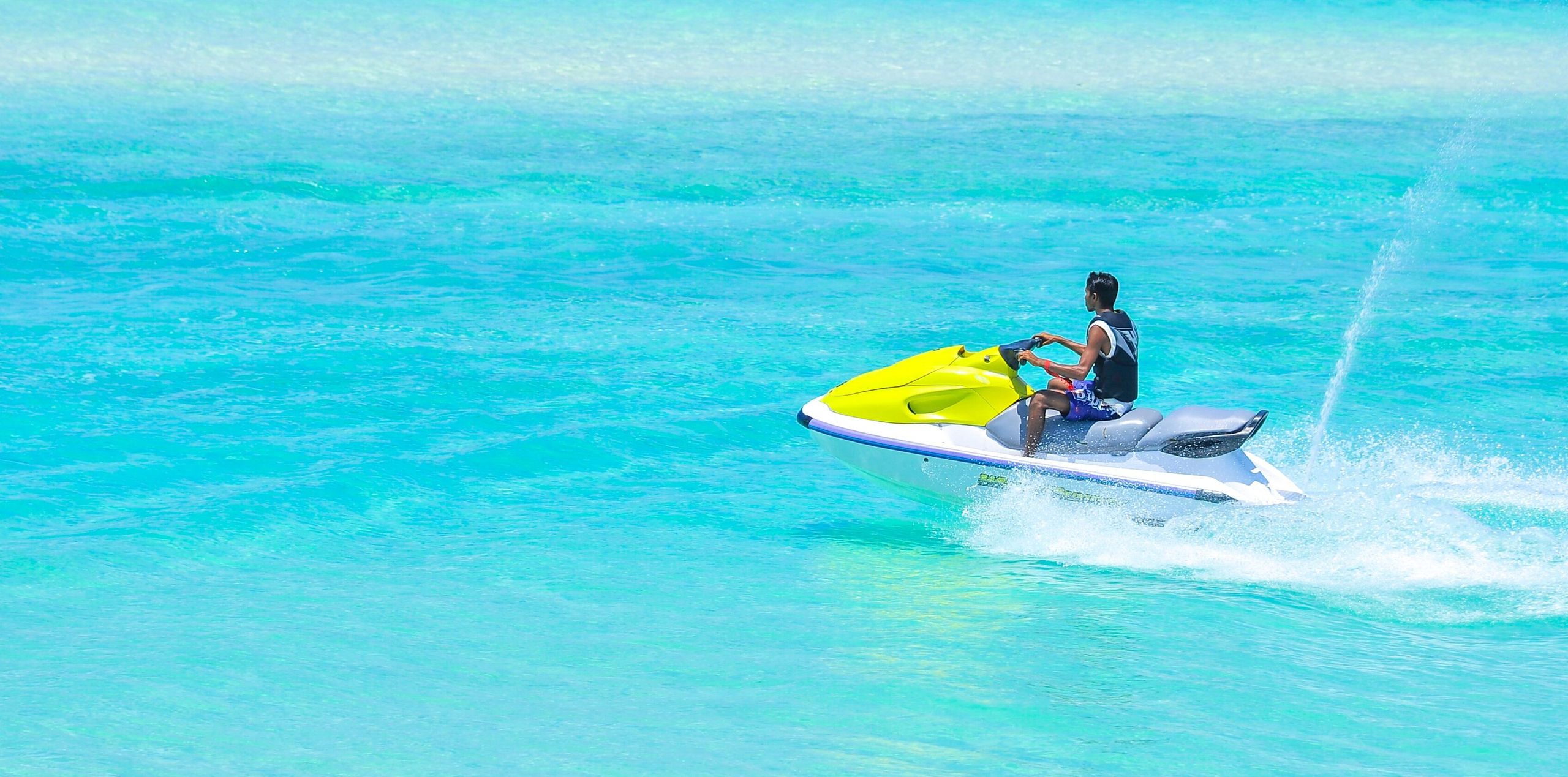 Rider pausing on a yellow Jet Ski on flat turquoise water