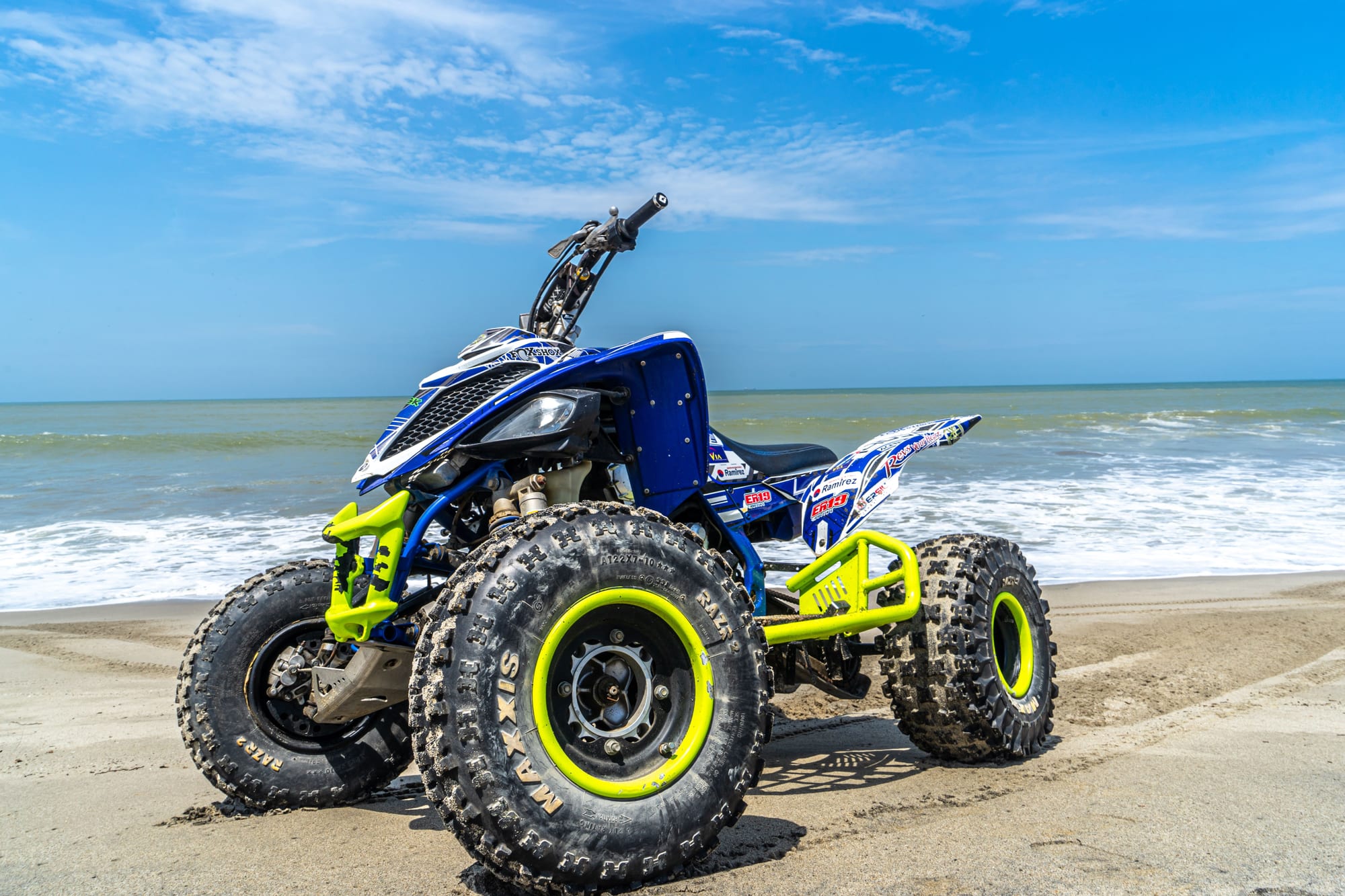 Low view of a blue and yellow sport quad on the beach, waves rolling in behind it