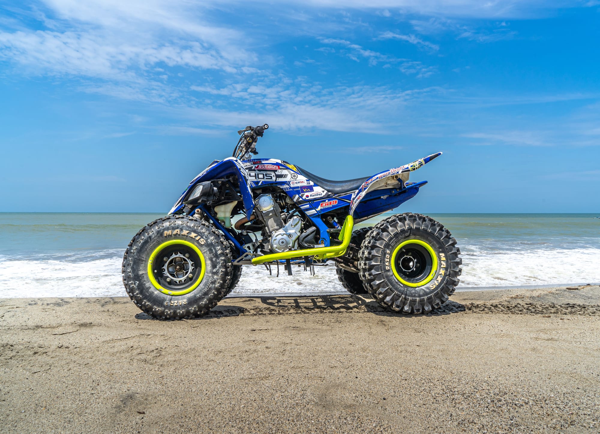 Side view of a blue and yellow sport quad on wet sand, surf breaking behind it