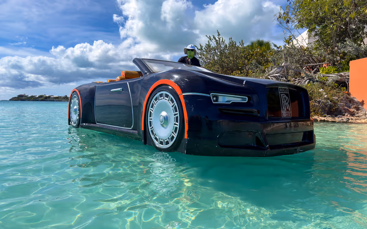 The black Rolls-Royce-styled 4-seater Jet Car in clear turquoise shallows beside a leafy shore