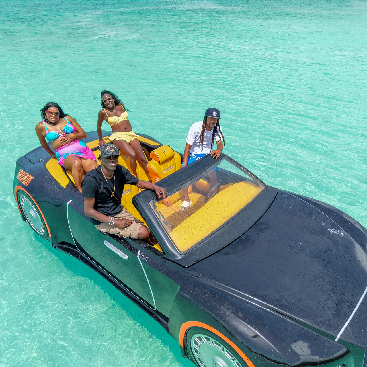 Four guests aboard the black and yellow 4-seater Jet Car, seen from above in shallow turquoise water