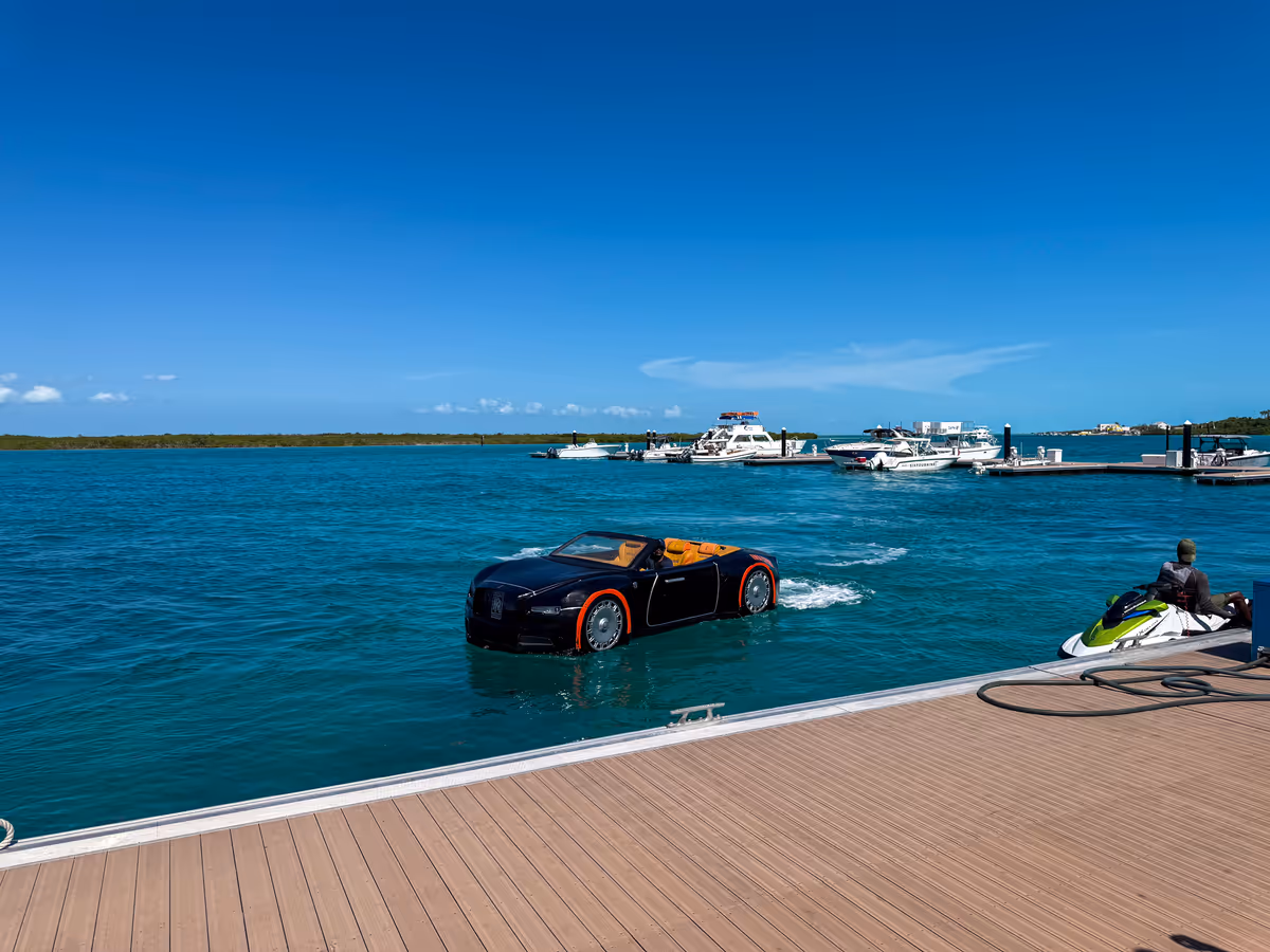 The black Jet Car on the water beside a dock, with moored boats across the channel behind it