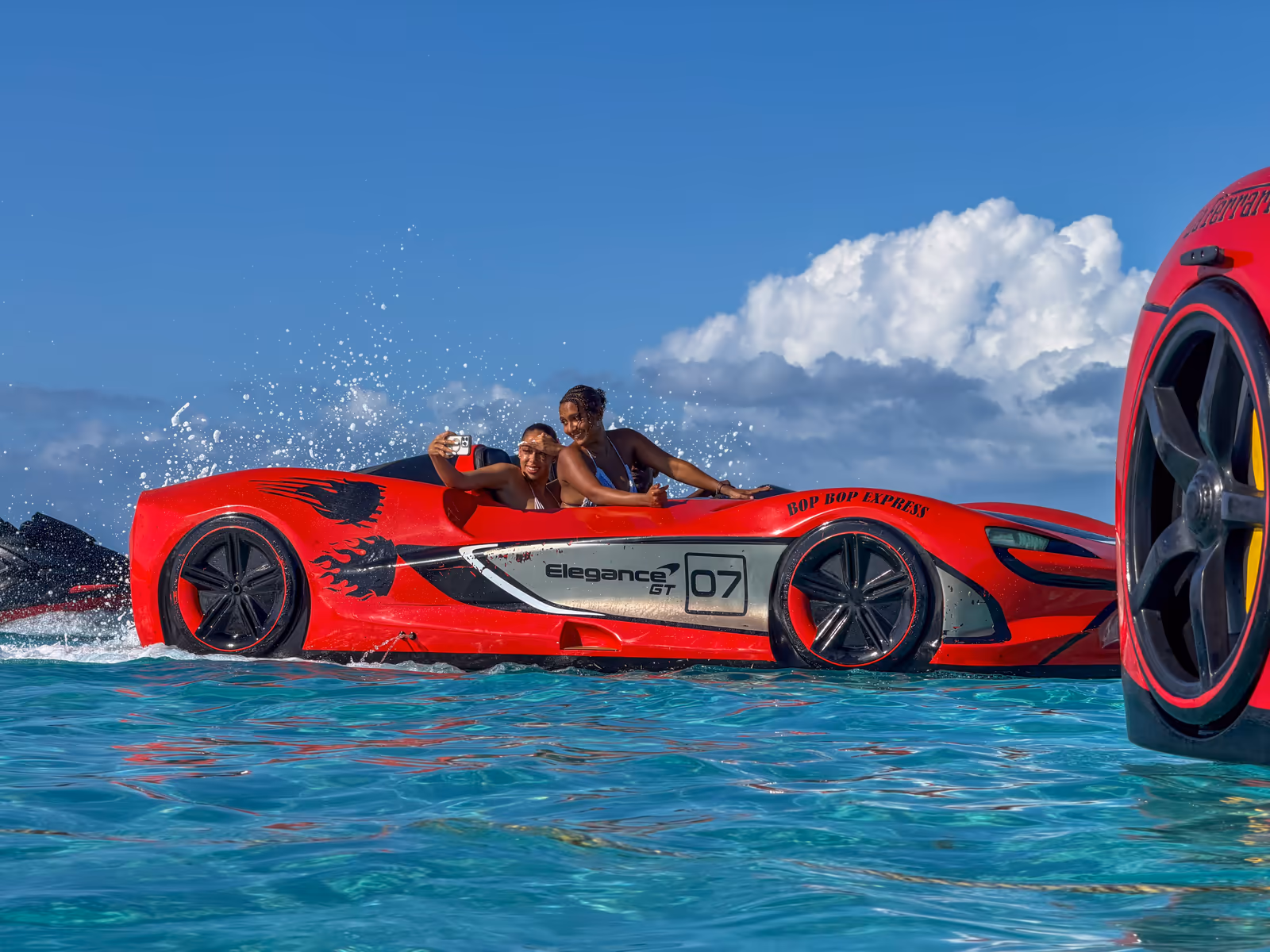Two guests driving the red Jet Car across turquoise water, spray coming off the front wheel