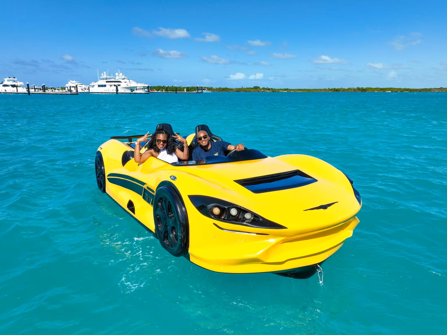 Two guests sitting in a bright yellow Jet Car on turquoise water, moored yachts behind