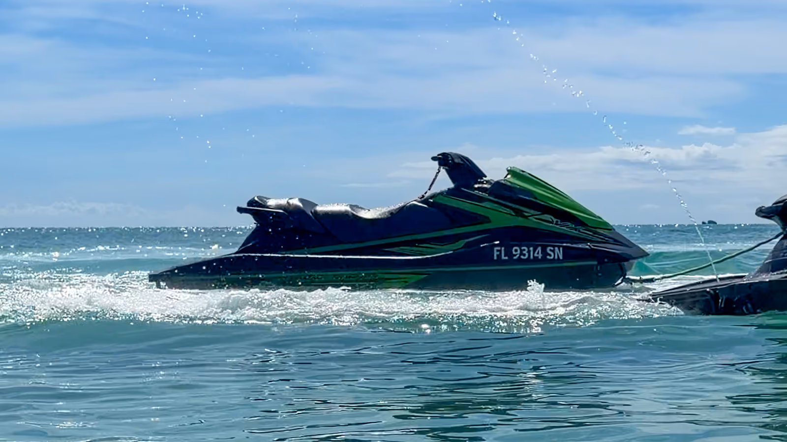 Two black and green Yamaha WaveRunners side by side on turquoise water, spray hanging in the air above them