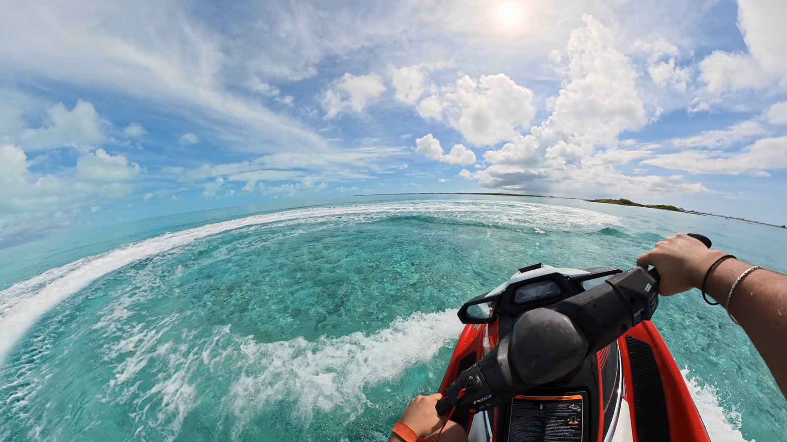 Rider view over the handlebars of a red Yamaha WaveRunner carving a curved wake across clear turquoise water