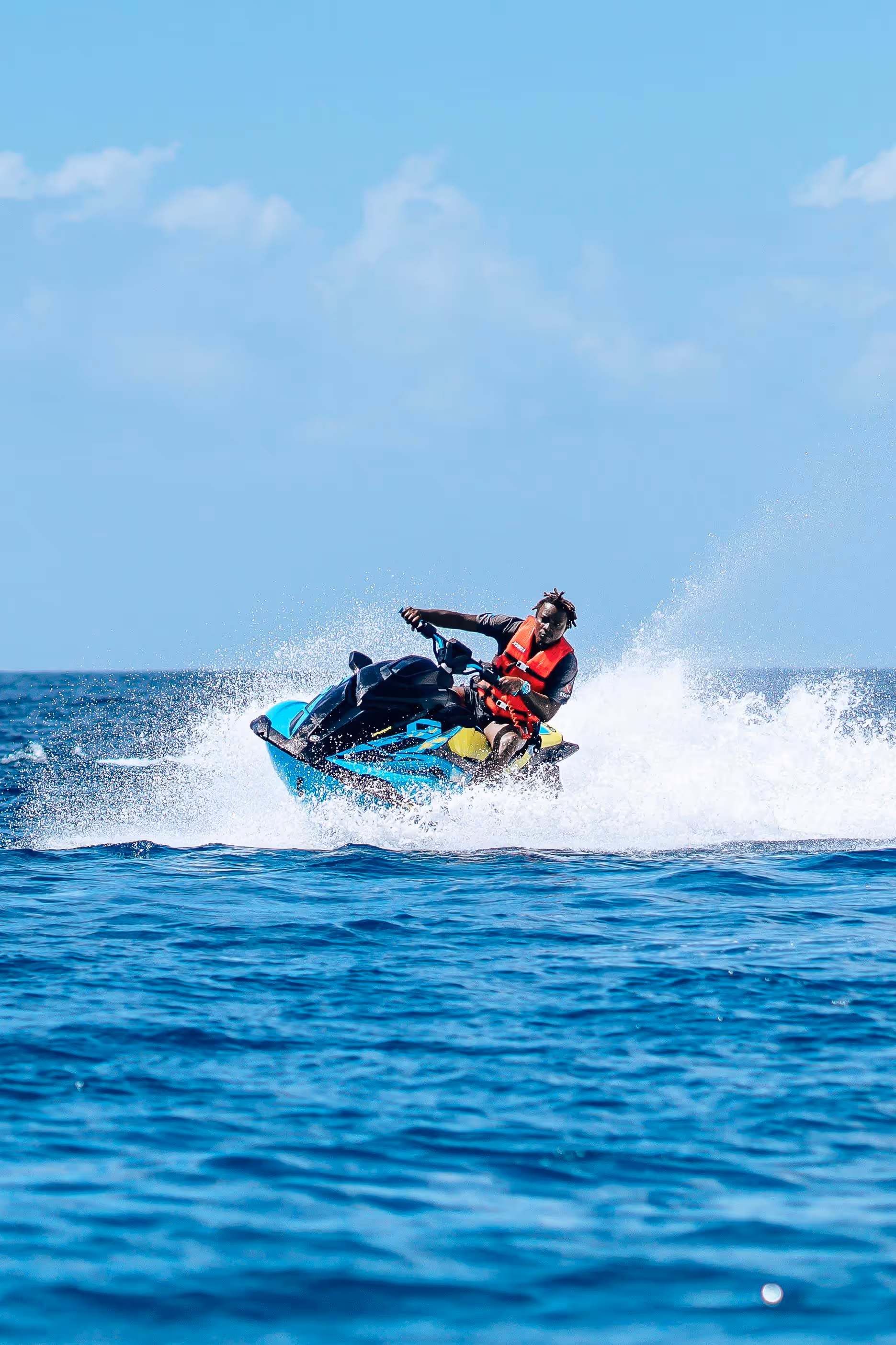 Rider in a life vest turning a teal Jet Ski hard, throwing spray across open water