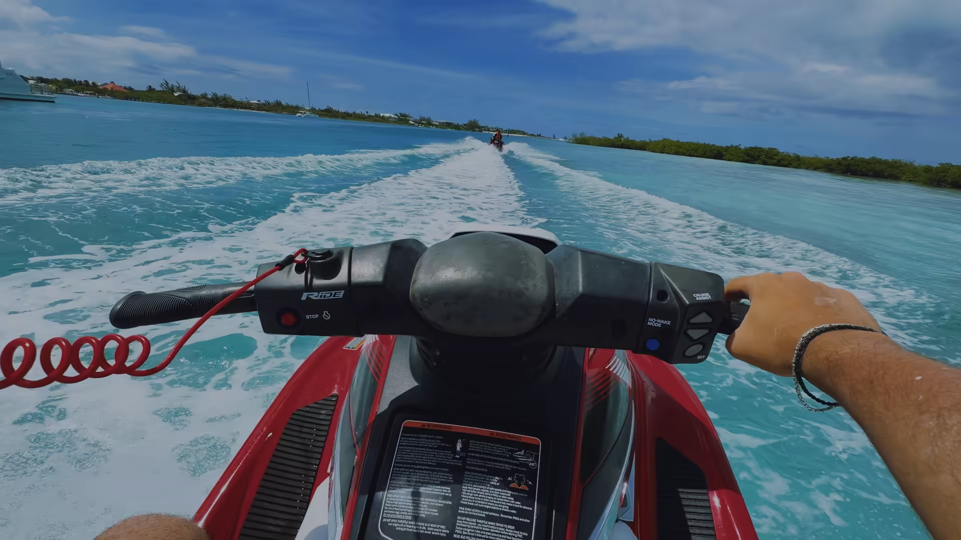The view from the seat of a red and white WaveRunner, with open water and a wake ahead
