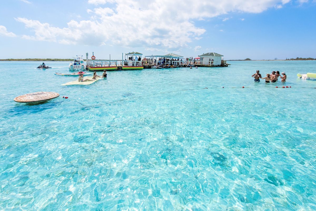 Guests swimming in waist-deep clear water beside the floating deck