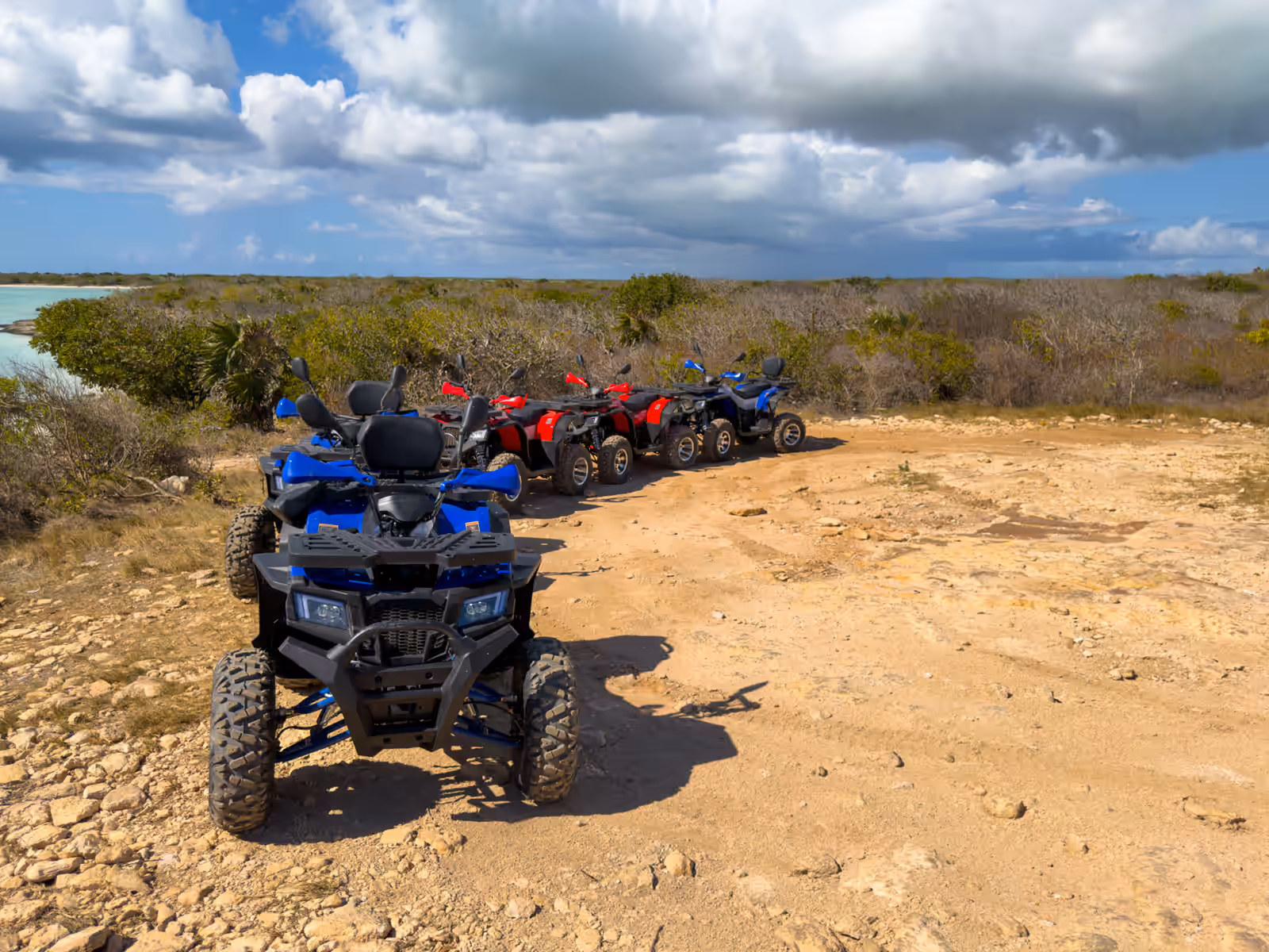 Quads parked on a dirt track through coastal scrub, a turquoise lagoon to the left