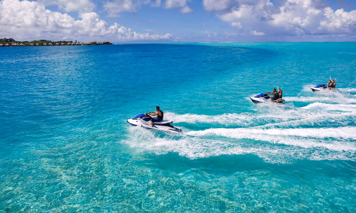 Three Jet Skis riding in line across bright turquoise water, a low shoreline in the distance