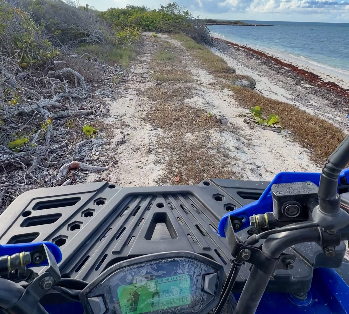 Rider view over the handlebars of a blue quad on a sand trail along the coast, reef and open sea to the right