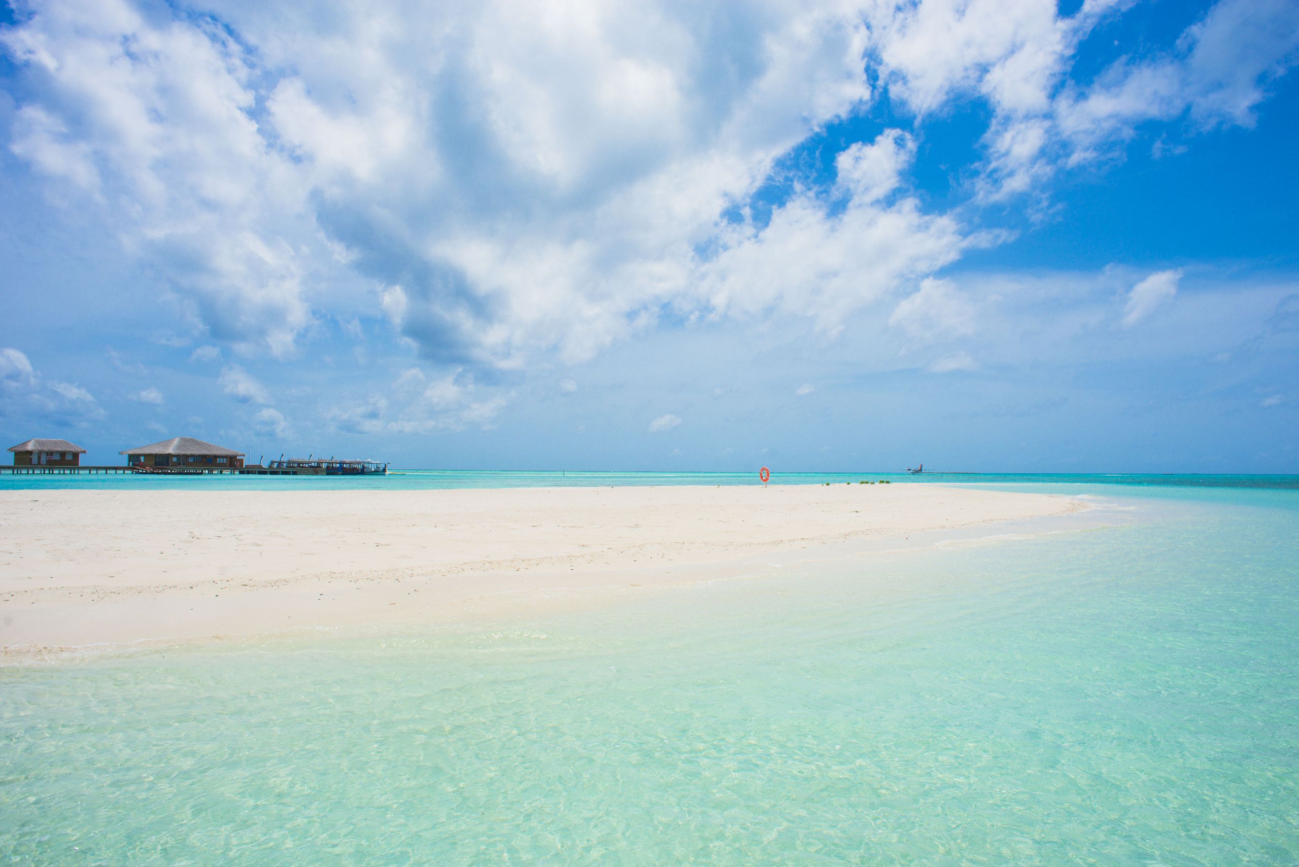 Empty white-sand beach with overwater villas on the horizon